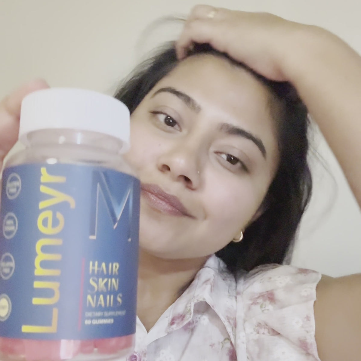 Creator holding a bottle of Lumeyr Hair Skin Nails gummies next to her face